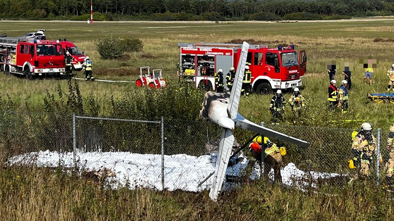 Einsatzkräfte der Feuerwehr stehen neben einem abgestürzten Kleinflugzeug.