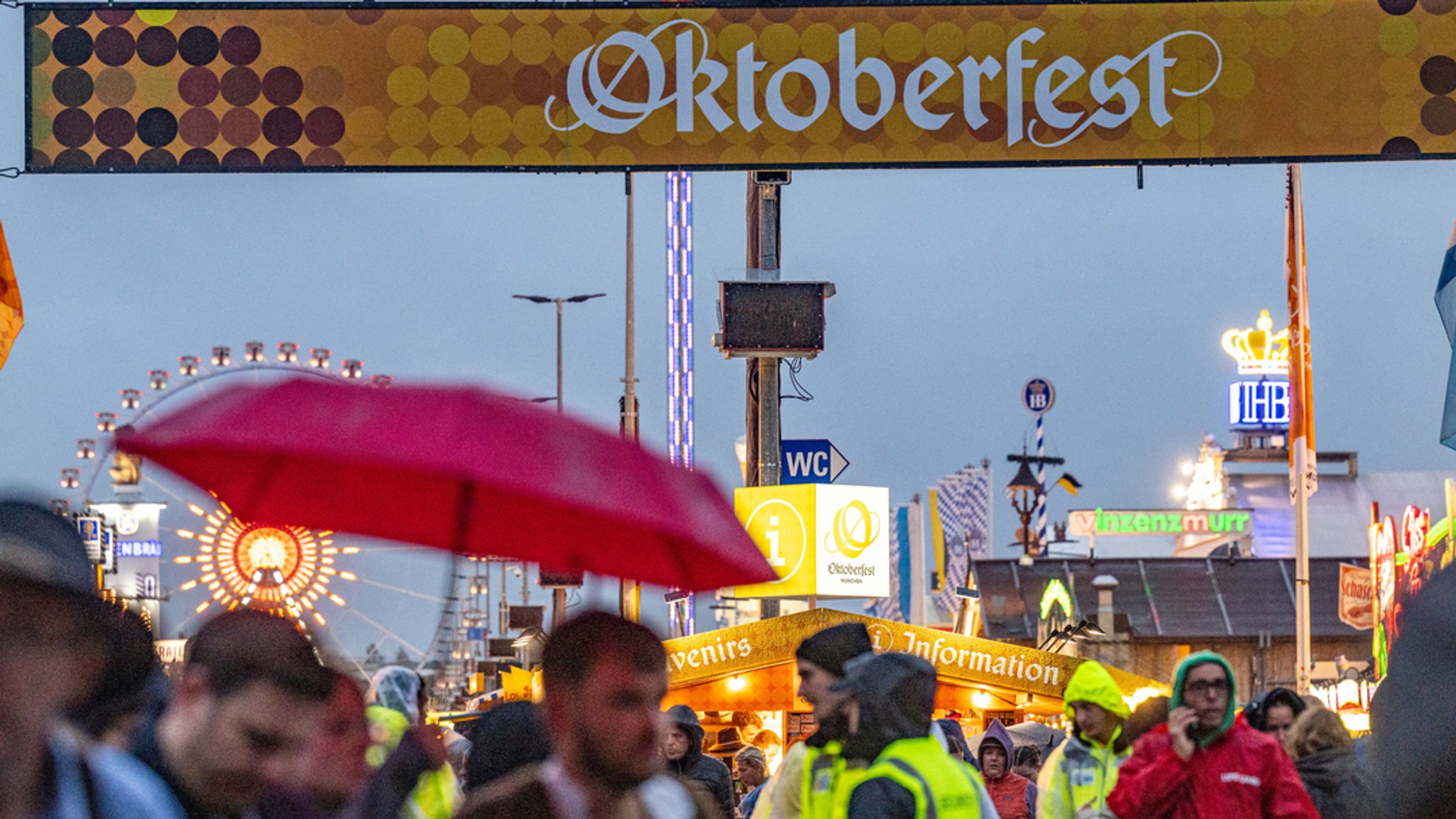 Besucher des Oktoberfestes stehen mit einem Schirm am Eingang des Festgeländes.