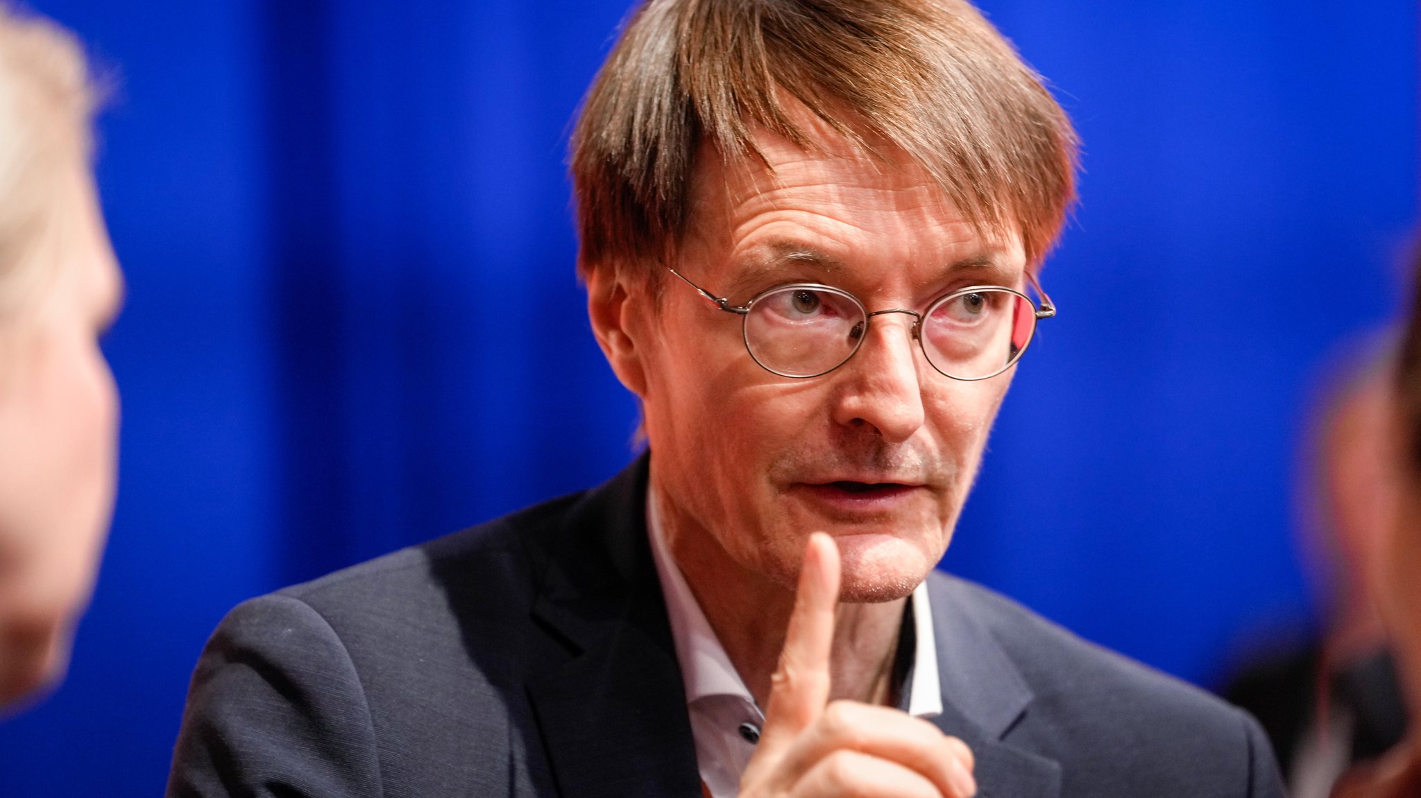 Bundesgesundheitsminister Karl Lauterbach sitzt mit ernster Miene und erhobenem Zeigefinger beim SPD-Bundesparteitag im Plenum in Berlin.