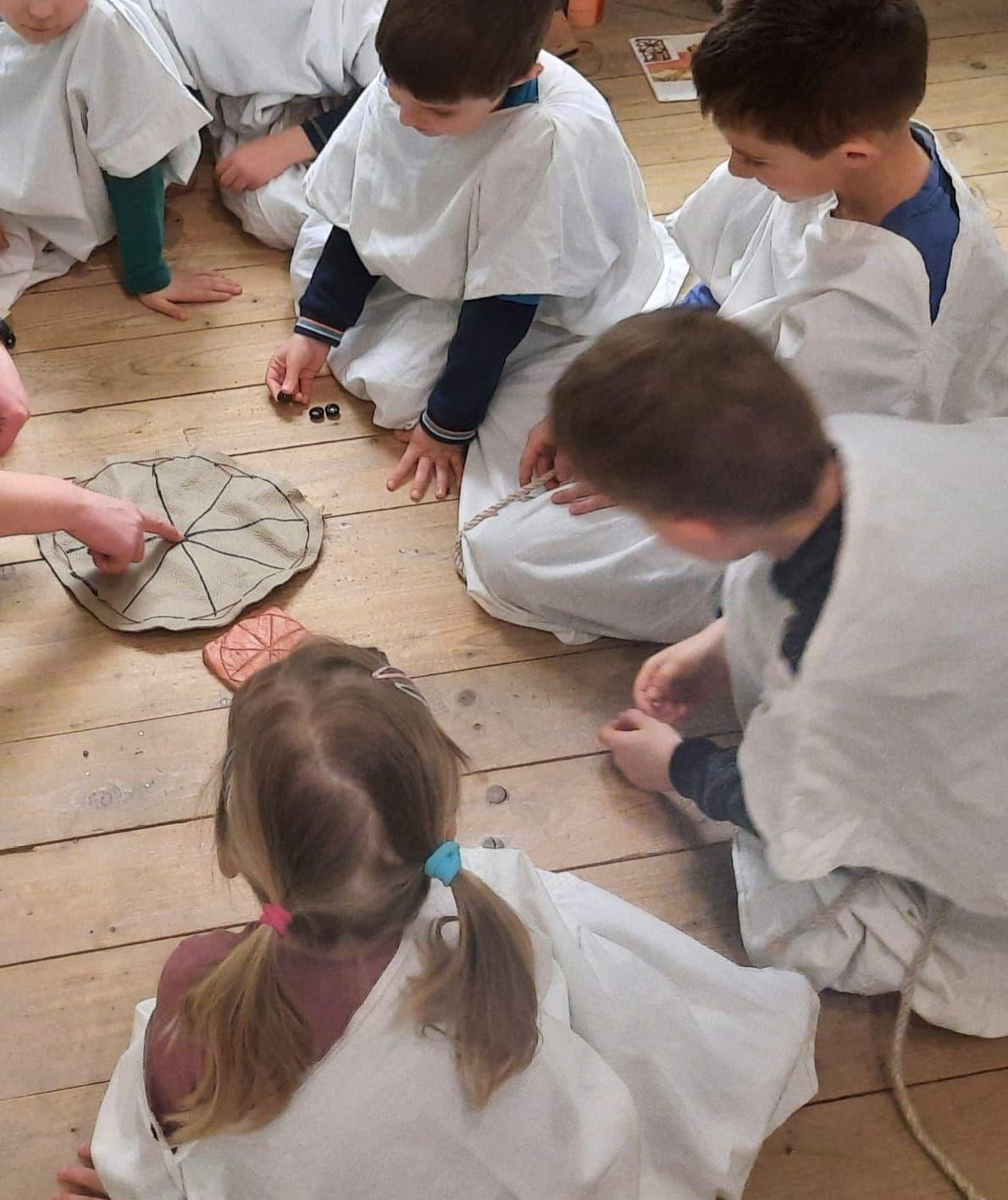 Eine Gruppe von Schülern in Römerkostümen spielt einen Vorläufer des heutigen Mühle-Spiels.