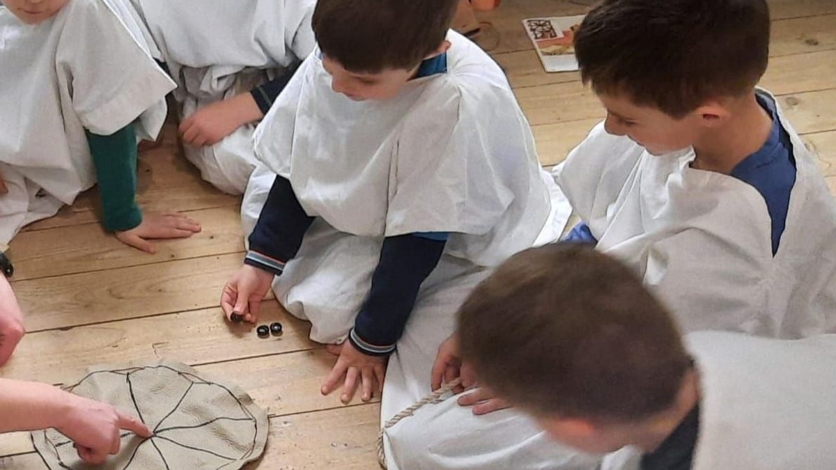 Eine Gruppe von Schülern in Römerkostümen spielt einen Vorläufer des heutigen Mühle-Spiels.