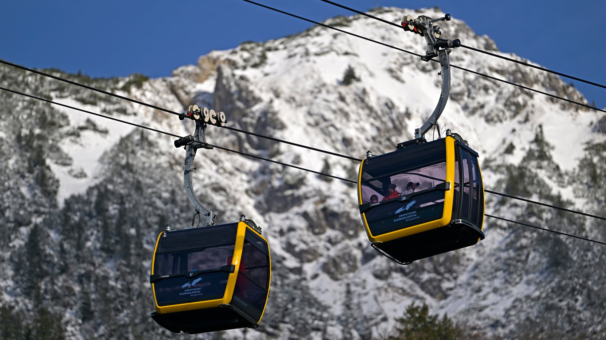 Gondeln der Nebelhornbahn fahren zum Gipfel. Im Hintergrund schneebedeckte Felsen.