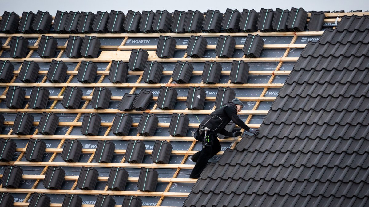 Ein Dachdeckermeister setzt eine Dachpfanne auf der Dachfläche eines Hauses.
