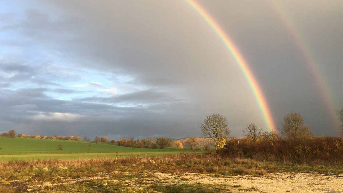 In einer Landschaft zeigt sich ein Regenbogen an einem abklingenden Gewitterhimmel.