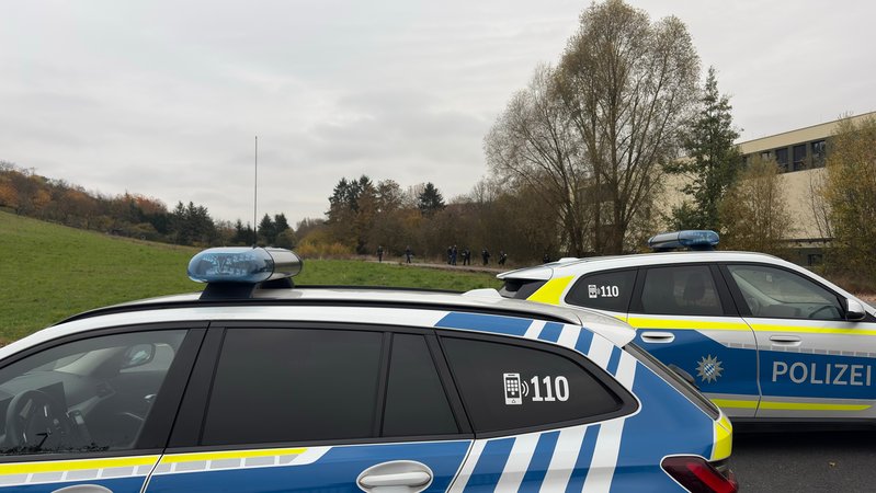 Zwei Polizeiautos stehen an einem Feldweg, im Hintergrund sind Polzisten und Polizistinnen zu sehen. | Bild: News 5 Zwei Polizeiautos stehen an einem Feldweg, im Hintergrund sind Polzisten und Polizistinnen zu sehen.