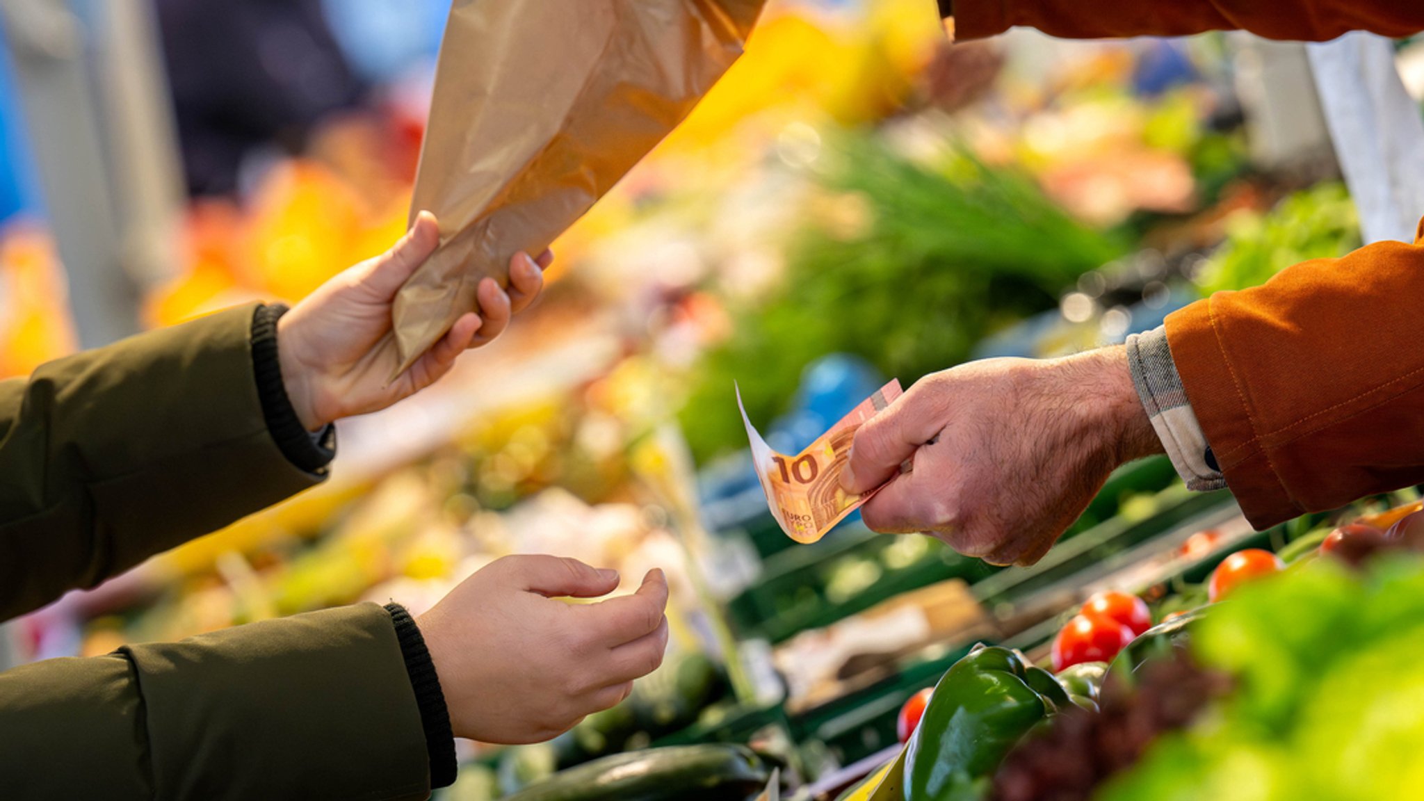 An einem Marktstand wird mit Bargeld eingekauft. 