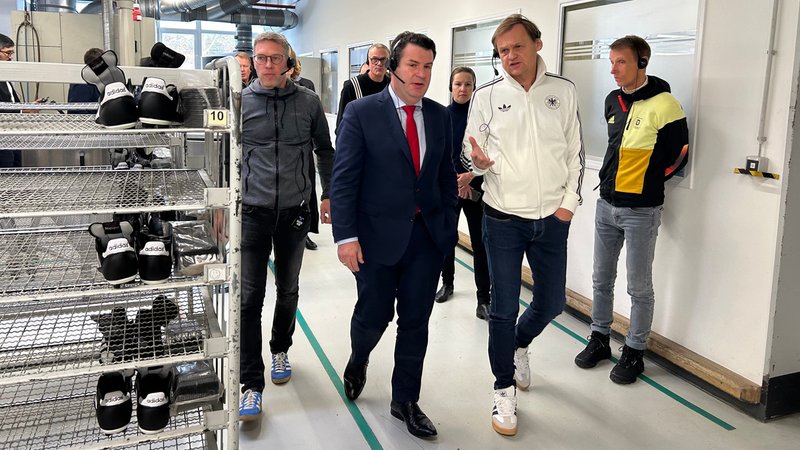 Hubertus Heil geht mit Adidas-Chef Björn Gulden durch den Gang eines Produktionswerks.