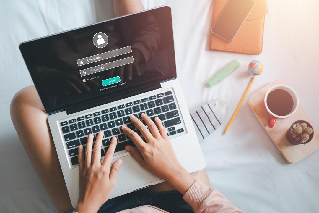 Eine Hand tippt auf der Tastatur das Login und Passwort auf dem Laptop-Bildschirm ein.