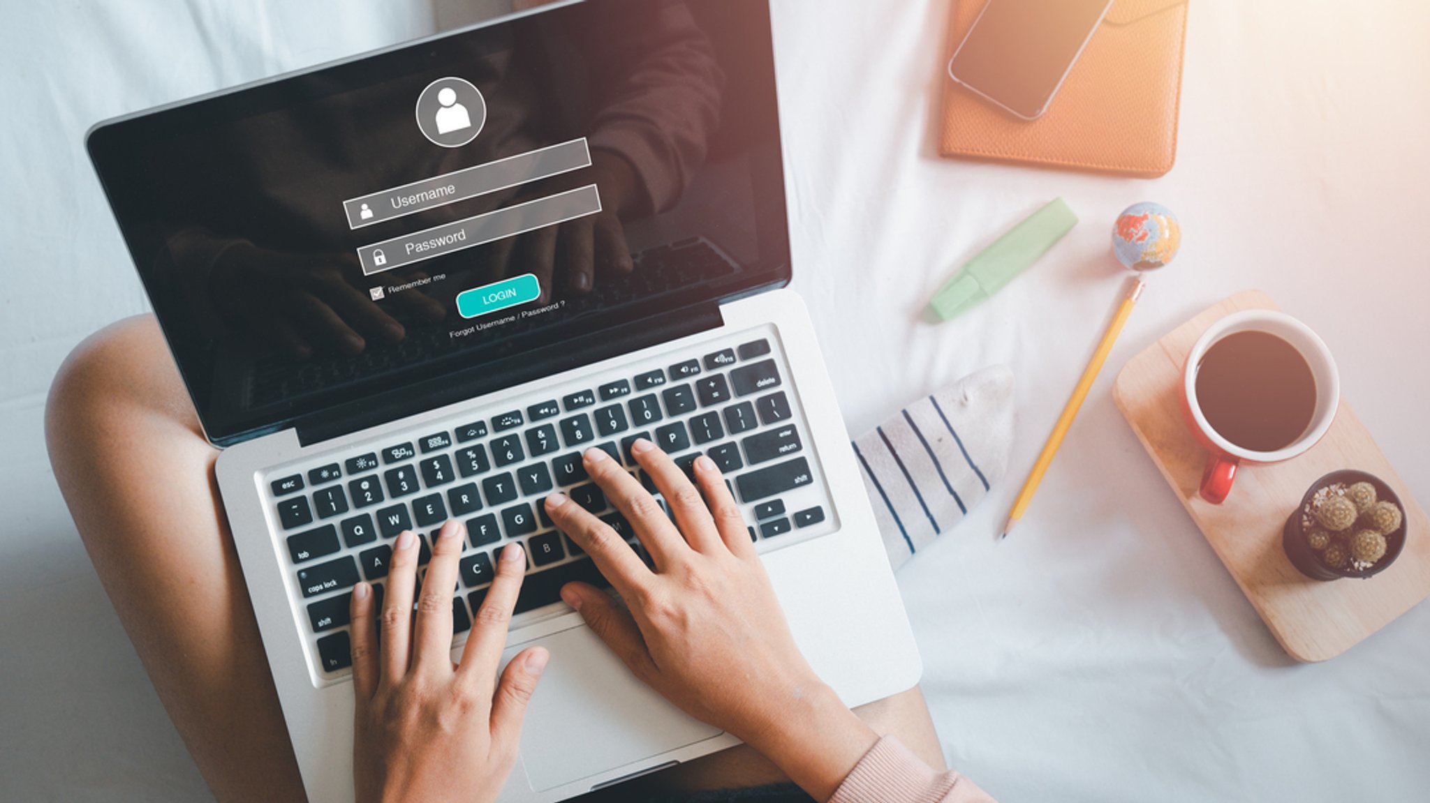 Eine Hand tippt auf der Tastatur das Login und Passwort auf dem Laptop-Bildschirm ein.