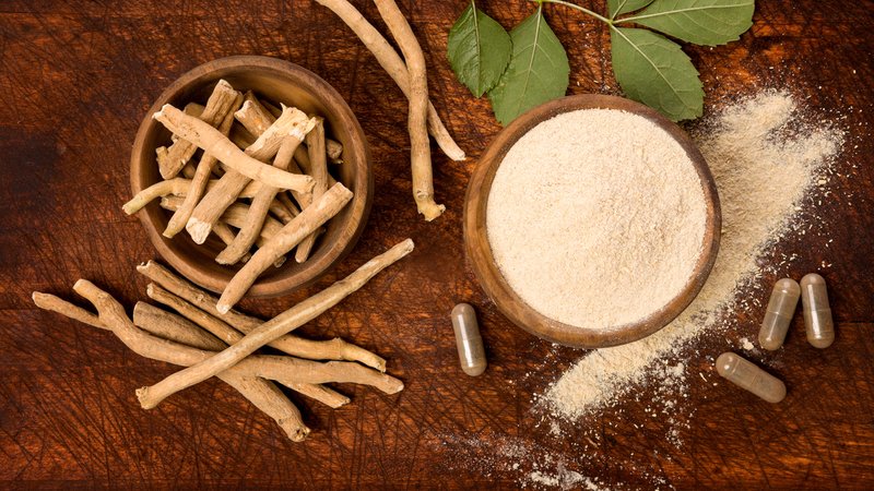 Auf einem Holztisch steht eine Schüssel mit Ashwagandha-Pulver, daneben liegen Ashwagandha-Wurzeln und Kapseln mit einem Ashwagandha-Präparat. | Bild: picture alliance / Zoonar | Eskymaks Auf einem Holztisch steht eine Schüssel mit Ashwagandha-Pulver, daneben liegen Ashwagandha-Wurzeln und Kapseln mit einem Ashwagandha-Präparat.