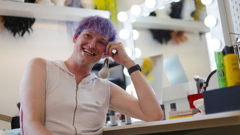 David Spectra Jeldrikl Blackwell sitzt vor einem Schminktisch mit einem Schminkpinsel in der Hand. | Bild: BR/Isabel Pogner David Spectra Jeldrikl Blackwell sitzt vor einem Schminktisch mit einem Schminkpinsel in der Hand.