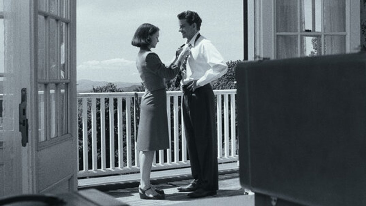 Frau bindet einem Mann auf einem Balkon die Krawatte.