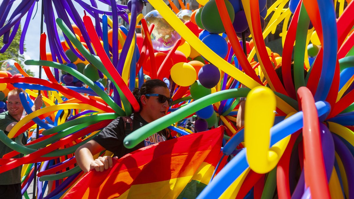 Viele bunte Luftballons bei der Gay Pride Parade in New York. Dazwischen eine Person mit dunkler Sonnenbrille
