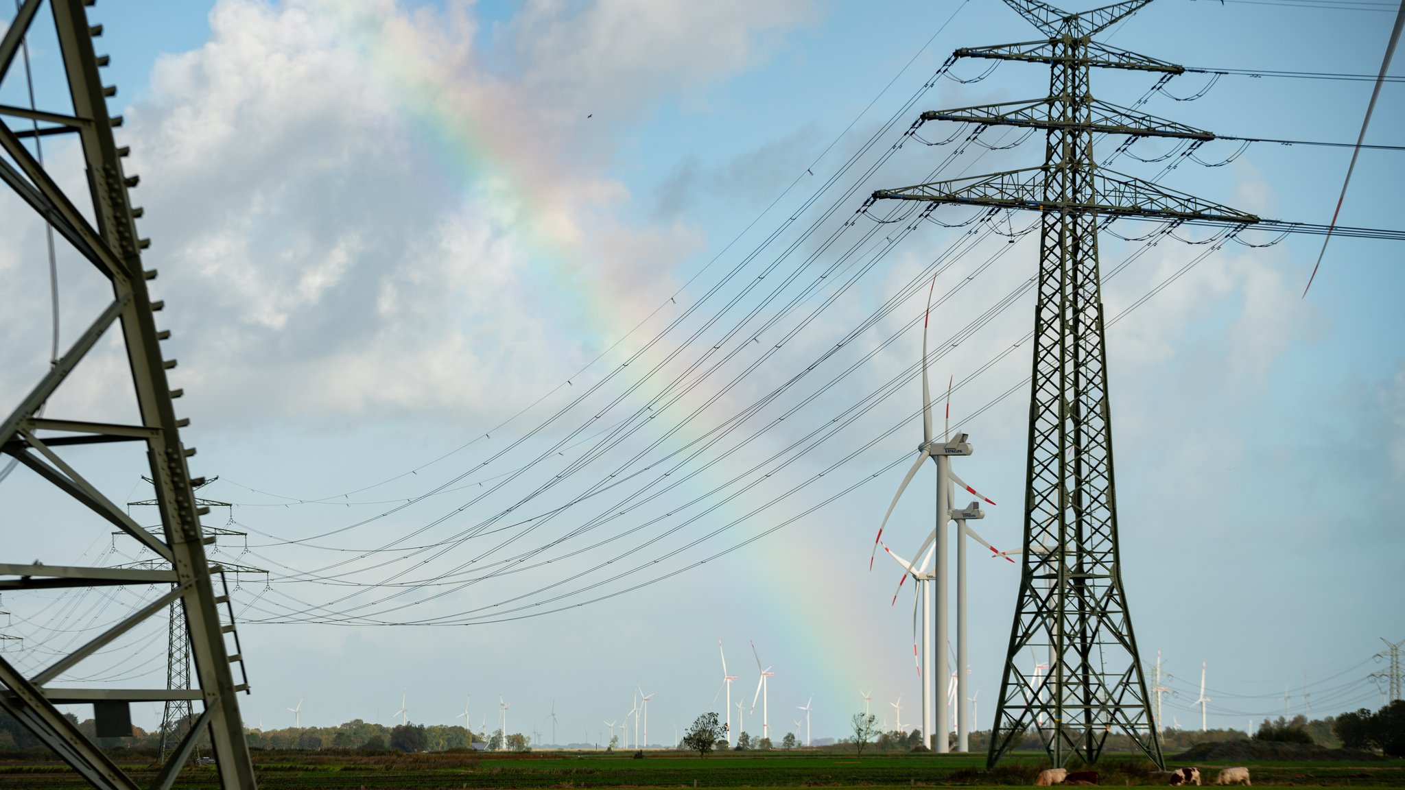 Ein Regenbogen zwischen Hochspannungsmasten und Windrädern.