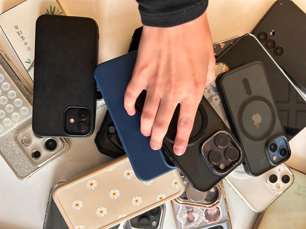 Hand legt ein Smartphone auf einen Stapel mit Smartphones auf einem Lehrerpult.