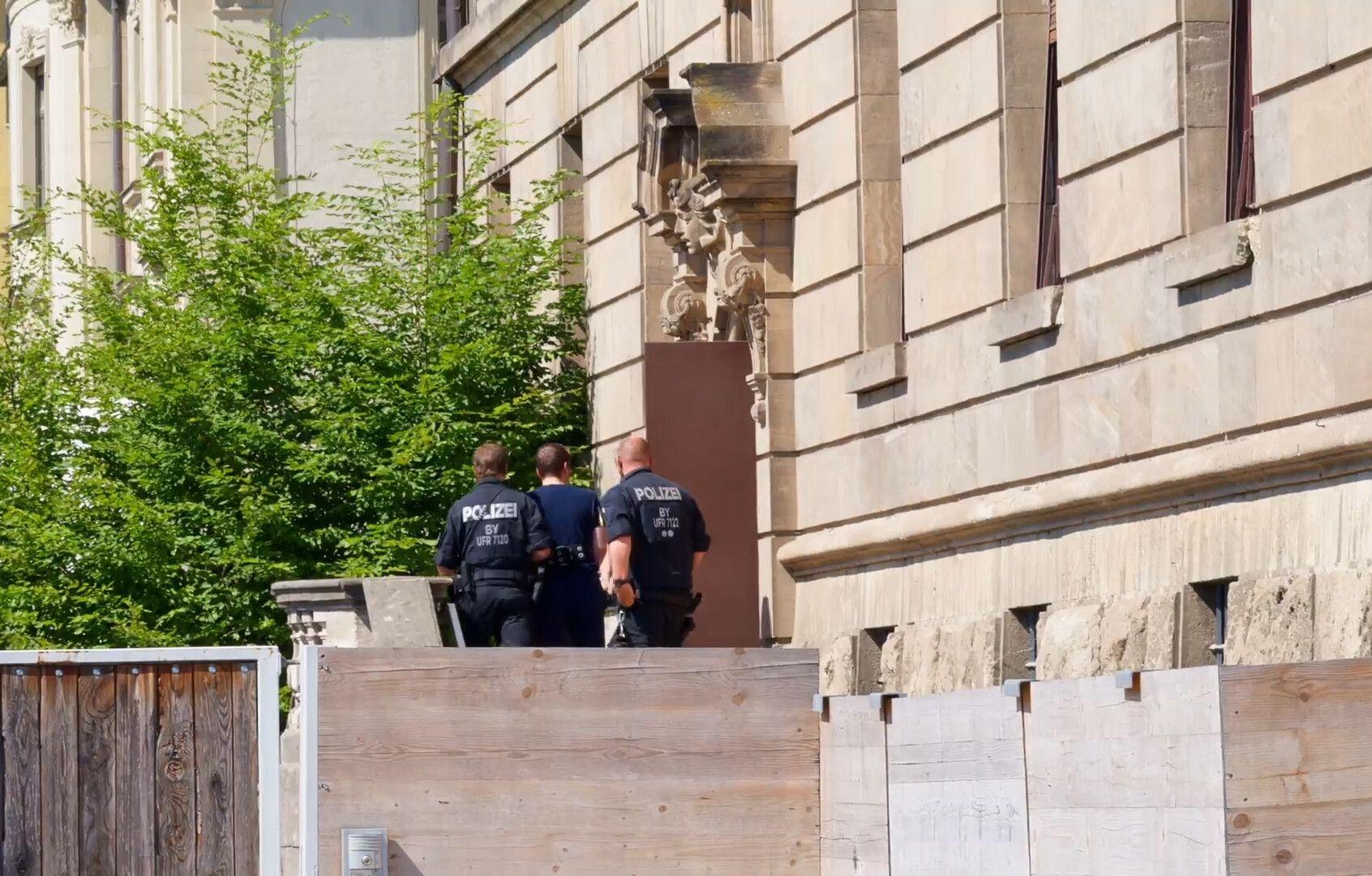 Archivbild 2. Juli 2025: Das Standbild aus einem Video zeigt, wie Polizeibeamte den Verdächtigen, der am Dienstag beim Stromversorger Überlandwerk Rhön in Mellrichstadt Kollegen mit einem Messer angegriffen, verletzt und eine tödlich verletzt haben soll, ins Gerichtsgebäude bringen. 
