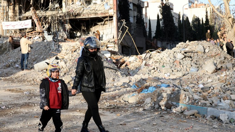 Eine Mutter läuft mit ihrem Sohn an einem durch US-israelische Angriffe zerstörtem Gebäude in Teheran vorbei (Archivbild: 21.3.2026) | Bild: Reuters/Alaa Al-Marjani Eine Mutter läuft mit ihrem Sohn an einem durch US-israelische Angriffe zerstörtem Gebäude in Teheran vorbei (Archivbild: 21.3.2026)