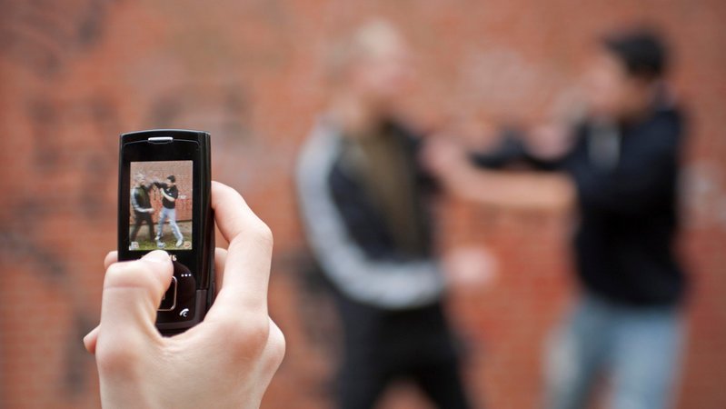 Gestellte Szene: Zwei Jungen prügeln sich auf dem Schulhof und werden dabei von einem dritten mit seinem Handy gefilmt. | Bild: picture alliance / imageBROKER | Siegfried Kuttig Gestellte Szene: Zwei Jungen prügeln sich auf dem Schulhof und werden dabei von einem dritten mit seinem Handy gefilmt.