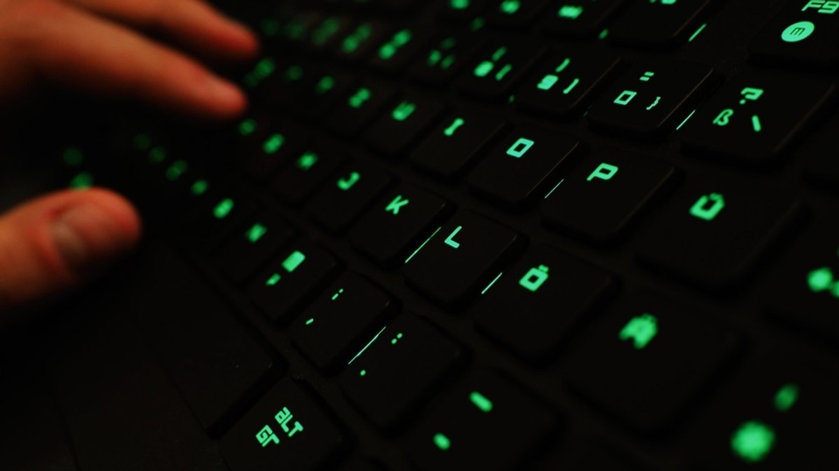 Ein Mann tippt auf einer beleuchteten Tastatur an einem Laptop.