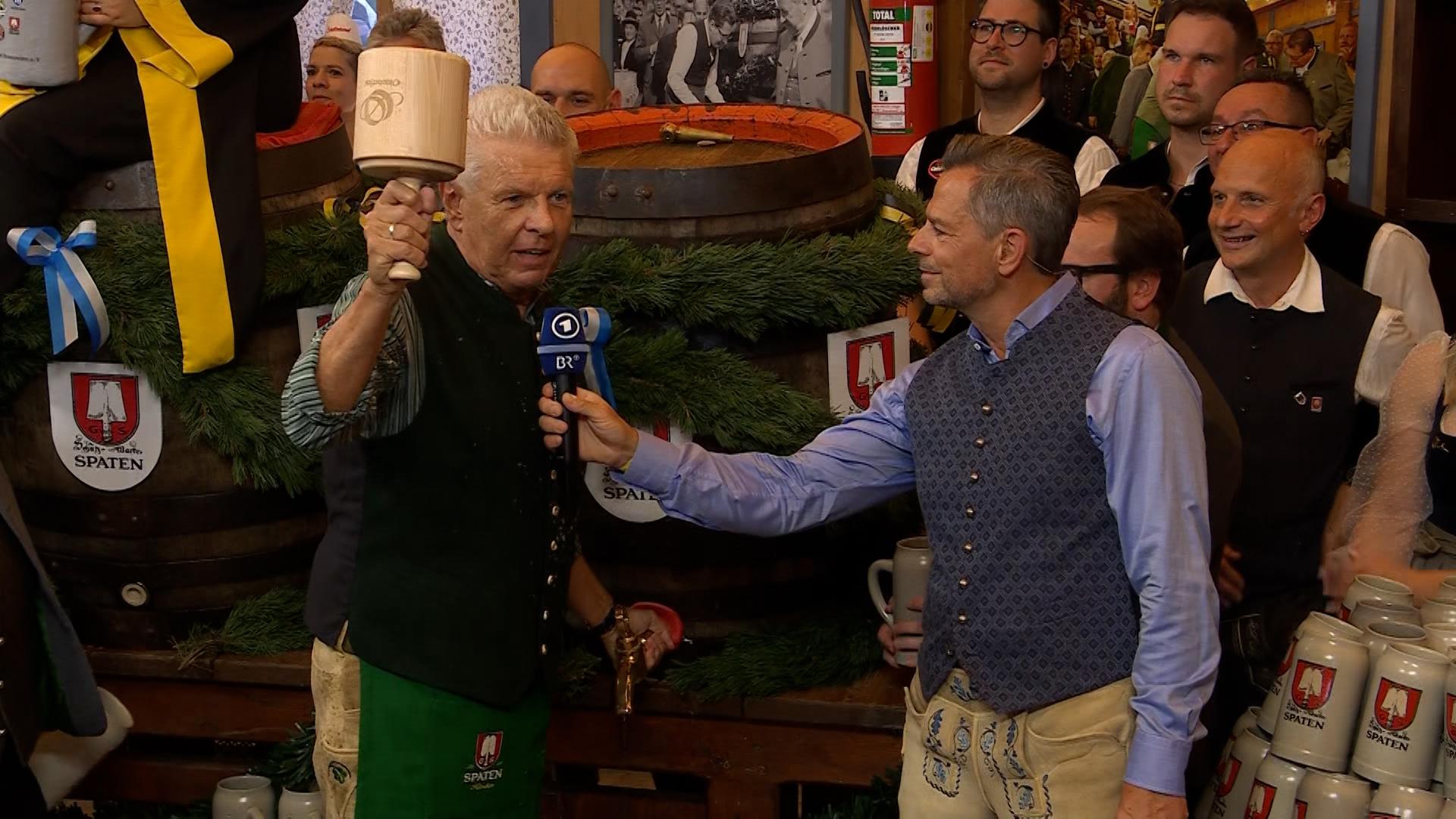 Oberbürgermeister Dieter Reiter am ersten Bierfass des 190. Oktoberfestes mit dem Anzapf-Schlegel in der Hand, BR-Moderator Michael Sporer hält ihm das Mikrofon hin.