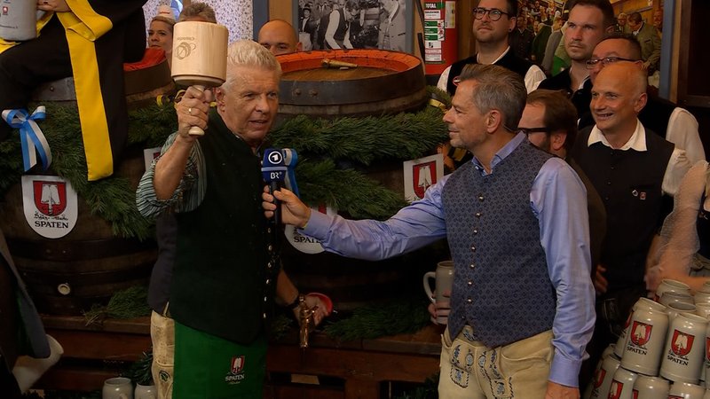 Oberbürgermeister Dieter Reiter am ersten Bierfass des 190. Oktoberfestes mit dem Anzapf-Schlegel in der Hand, BR-Moderator Michael Sporer hält ihm das Mikrofon hin. | Bild: Bayerischer Rundfunk 2025 Oberbürgermeister Dieter Reiter am ersten Bierfass des 190. Oktoberfestes mit dem Anzapf-Schlegel in der Hand, BR-Moderator Michael Sporer hält ihm das Mikrofon hin.