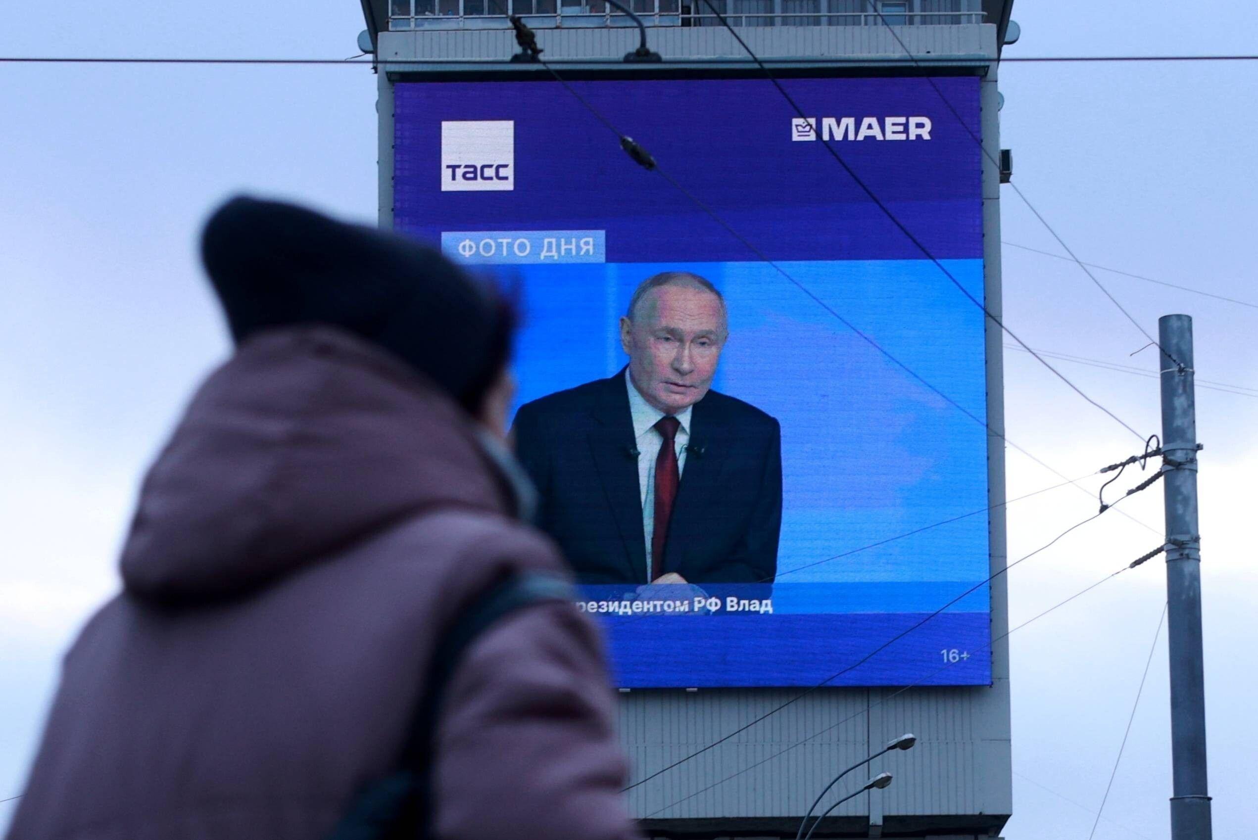 Passantin geht an einem Bildschirm vorbei, auf dem eine Putin-Pressekonferenz übertragen wird