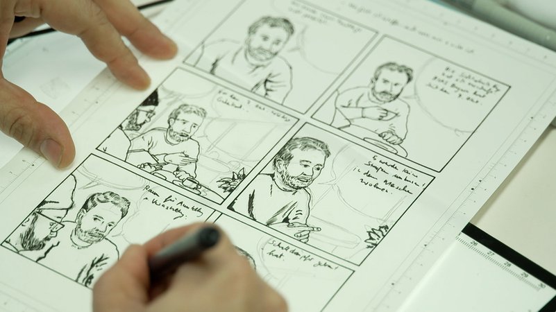 Ein Künstler sitzt an einem Schreibtisch und zeichnet. | Bild: BR/ Julia Demel Ein Künstler sitzt an einem Schreibtisch und zeichnet.