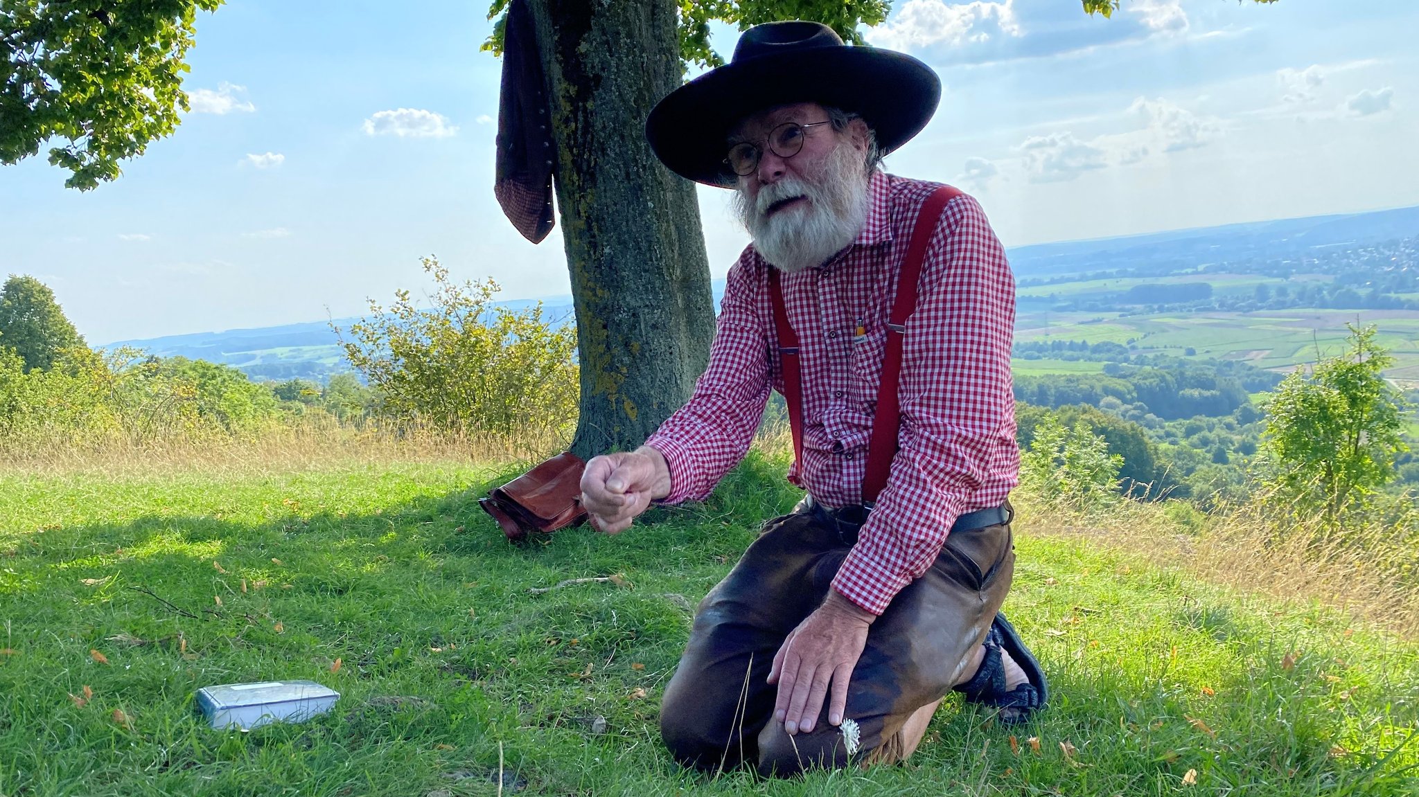 Ein Mann kniet im Gras unter einem Baum. 