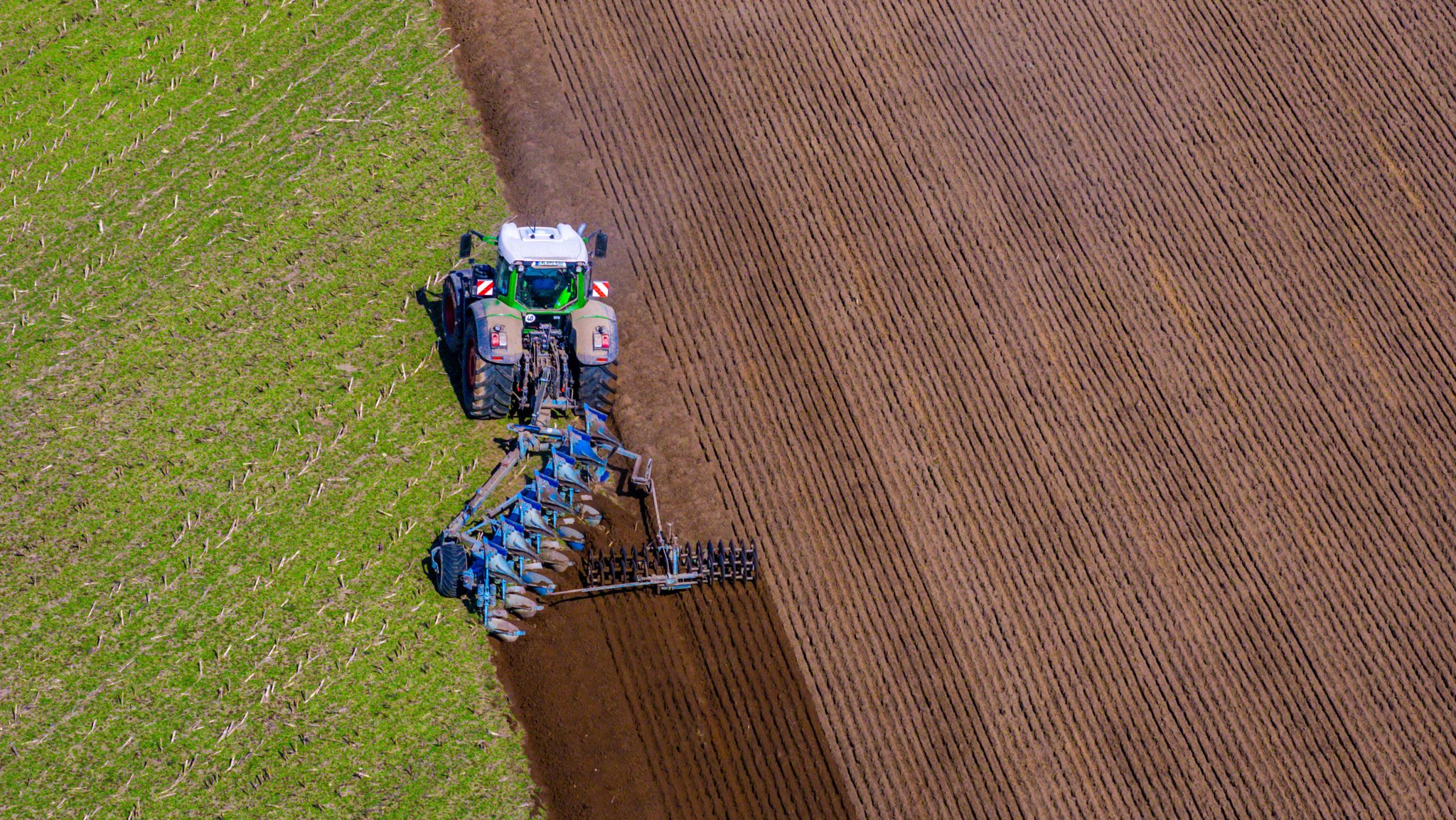 Ein Traktor zieht einen Pflug über einen Acker und bereitet das Feld auf die Aussaat in den nächsten Tagen vor (Symbolbild)