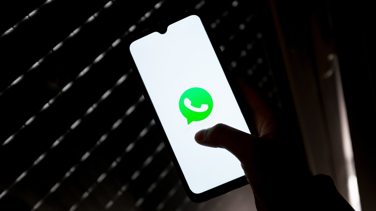 Ein WhatsApp-Logo leuchtet auf einem Handy vor einem dunklen Hintergrund.