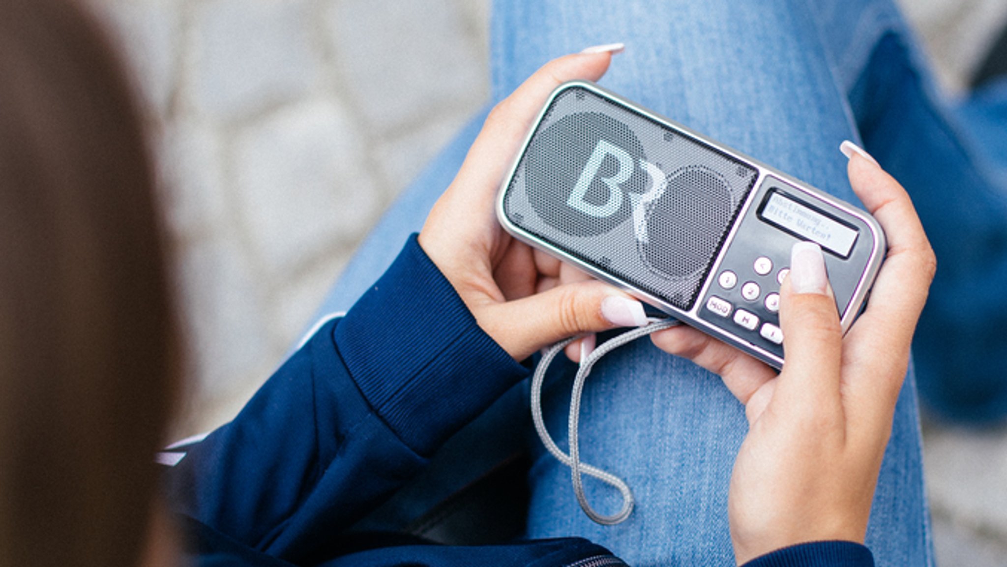 Eine Frau hat ein tragbares DAB Radio in der Hand.