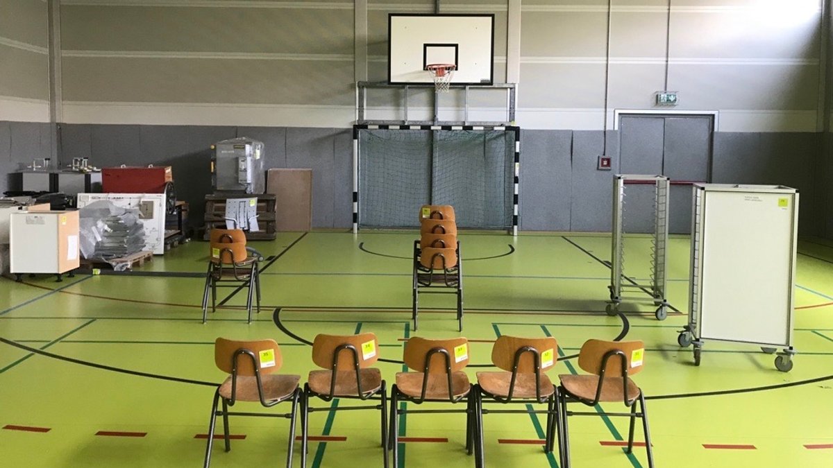 Eine Turnhalle mit grünem Boden, in dem Stühle und andere Gegenstände stehen.