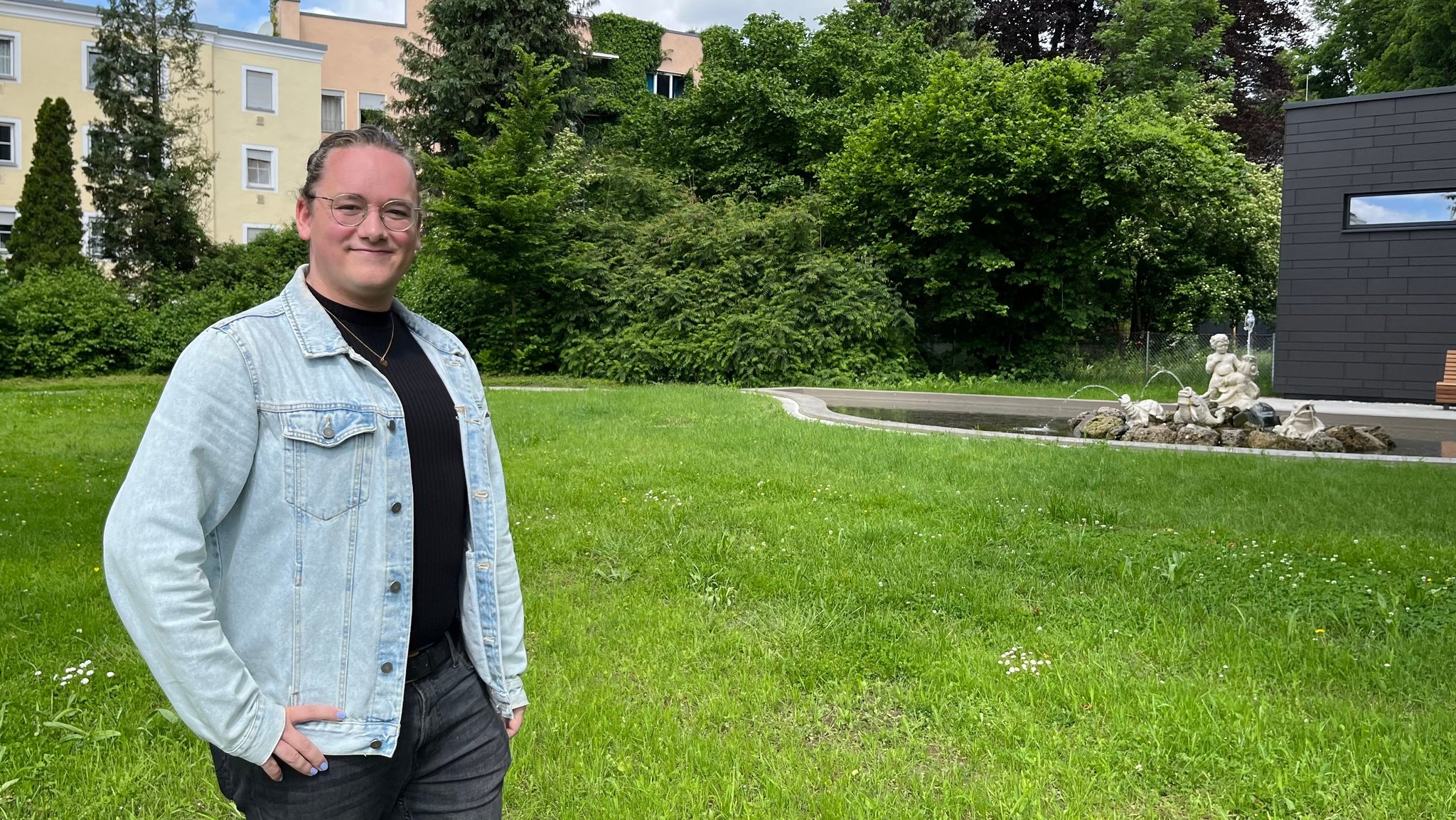 Sea Altmann steht mit Jeansjacke lächelnd im Park.