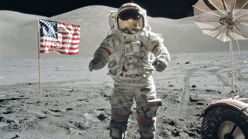 Gene Cernan, Kommandant der Apollo 17 im Dezember 1972, auf dem Mond, flankiert von amerikanischer Flagge und Mondfahrzeug.