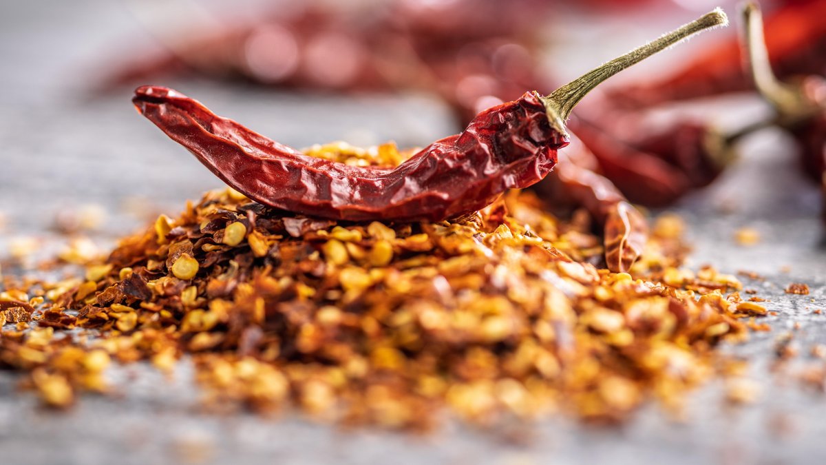 Eine Chilischote auf einem Häufchen Chiliflocken