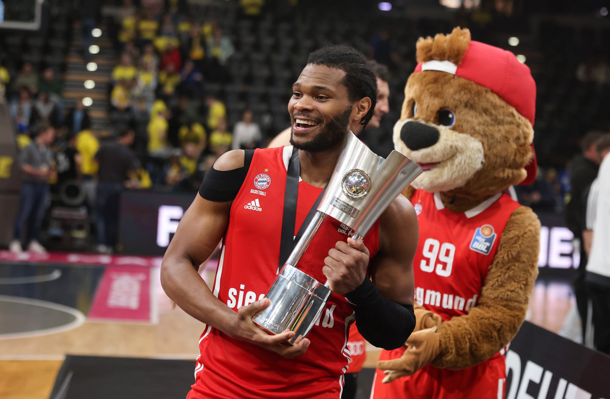 Nick Weiler-Babb (FC Bayern Basketball) mit Maskottchen und Pokal 2023