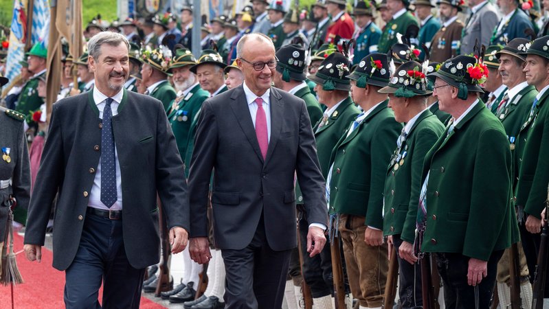 Bayerns Ministerpräsident Söder und Bundeskanzler Merz werden von einer Reihe Gebirgsschützen begrüßt. | Bild: picture alliance/dpa | Peter Kneffel Bayerns Ministerpräsident Söder und Bundeskanzler Merz werden von einer Reihe Gebirgsschützen begrüßt.