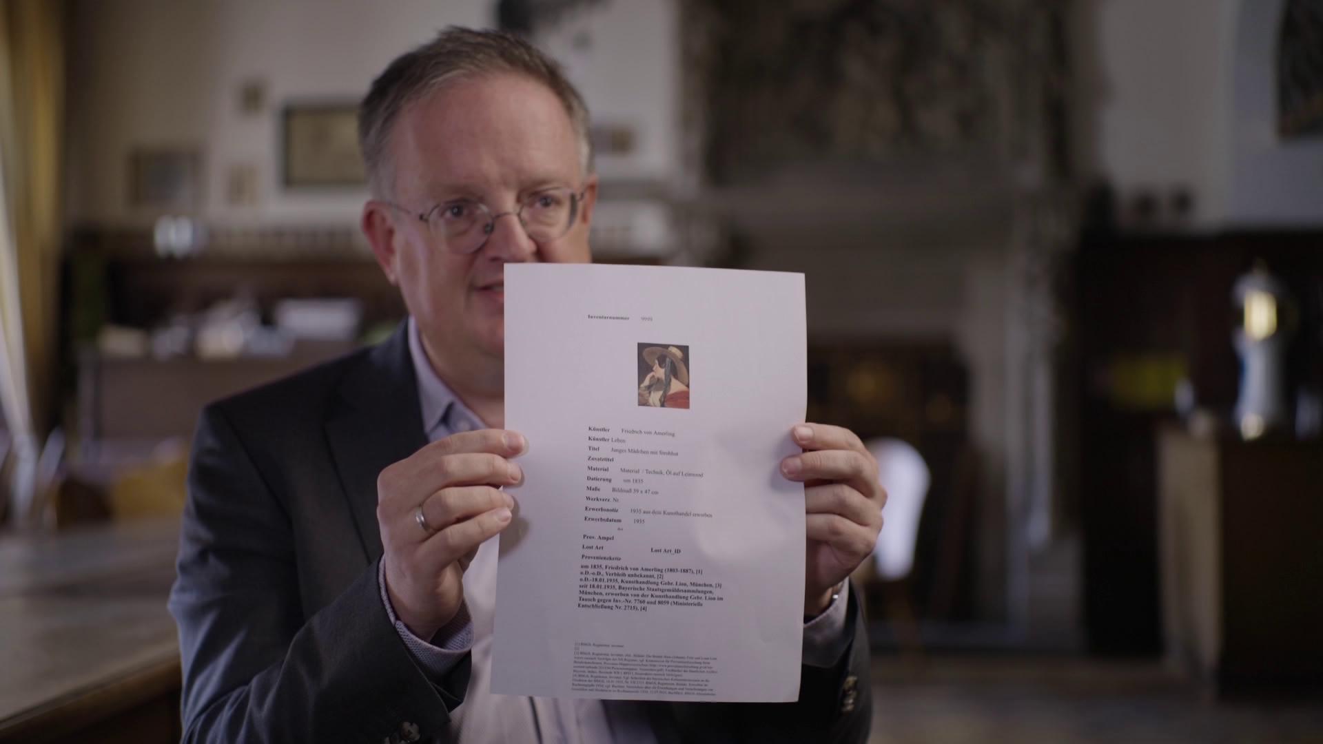 Rechtsanwalt Hannes Hartung hält Ausdruck in die Kamera, darauf klein zu sehen das "Mädchen mit Strohhut"