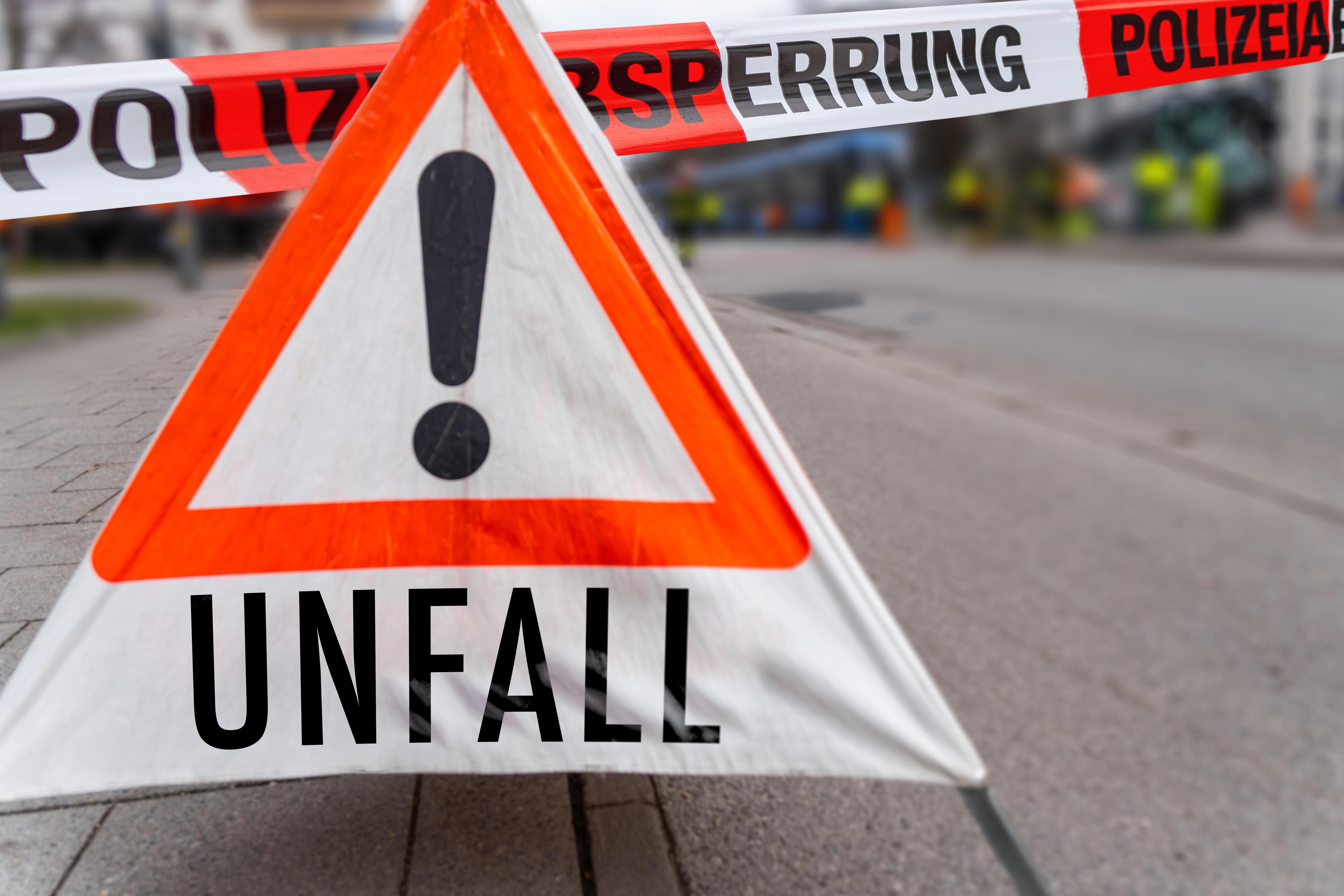 Ein Warnschild mit der Aufschrift "Unfall" neben Absperrband der Polizei.