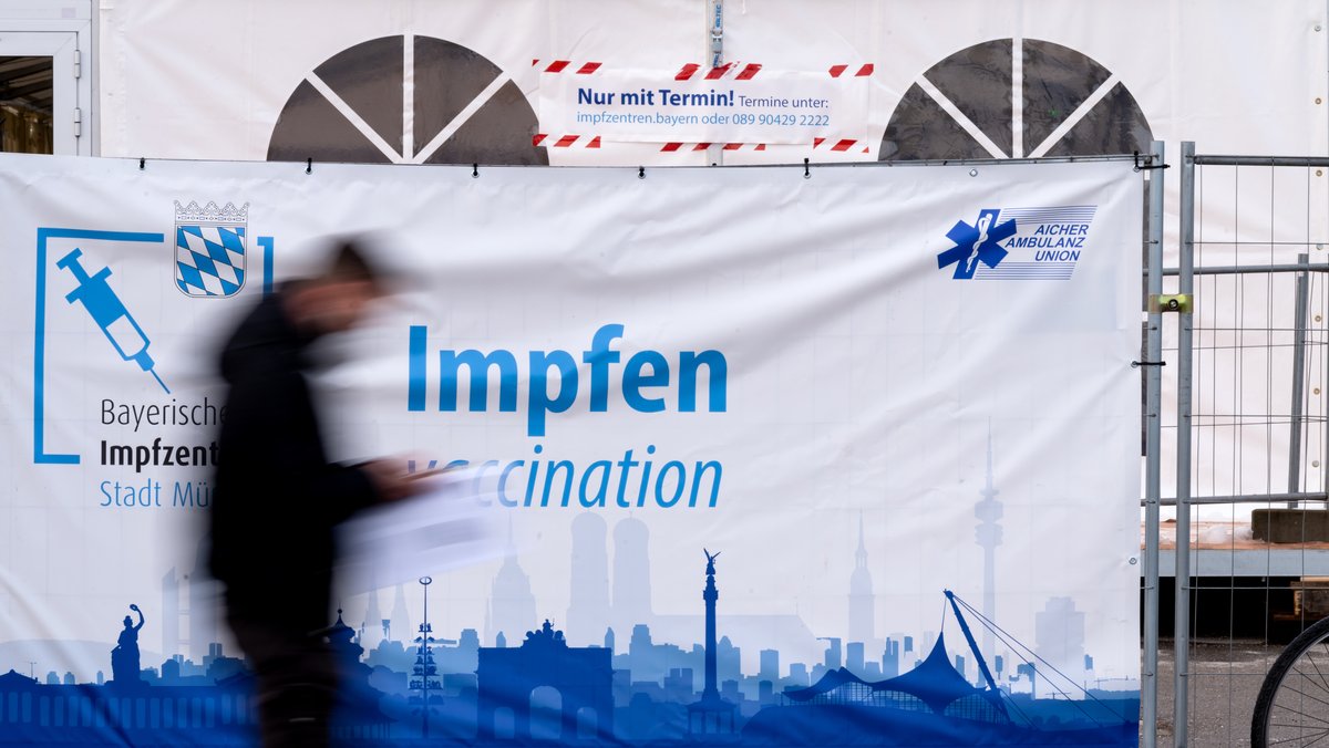 Ein Mann geht auf der Theresienwiese in München an einem Plakat der Aufschrift "Impfen" vorbei.