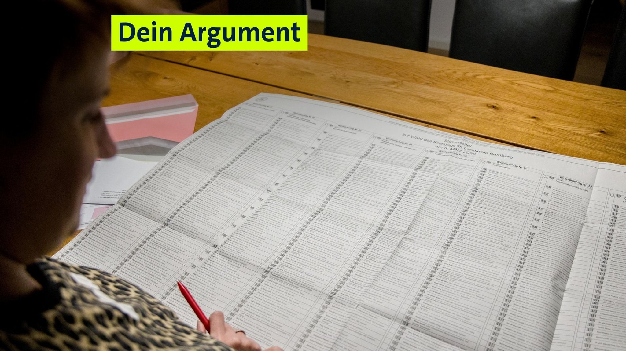 Eine Frau sitzt vor einem großen Stimmzettel zu einer Gemeinderatswahl mit vielen Kandidaten. 