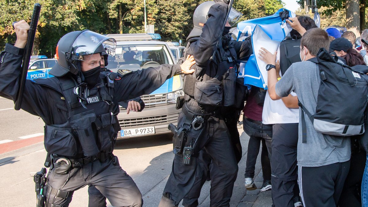 Polizisten mit Schlagstöcken stehen Demonstranten gegenüber