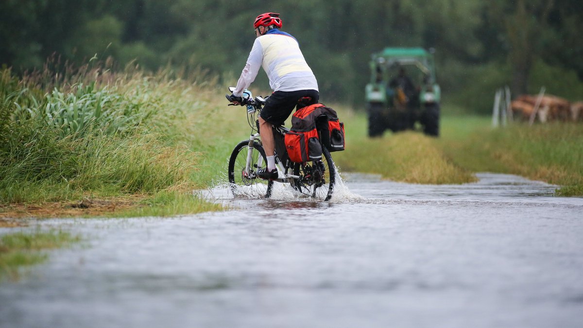Archivbild: Ein Radfahrer ist im Regen auf einem überfluteten Radwanderweg an der Donau unterwegs. 