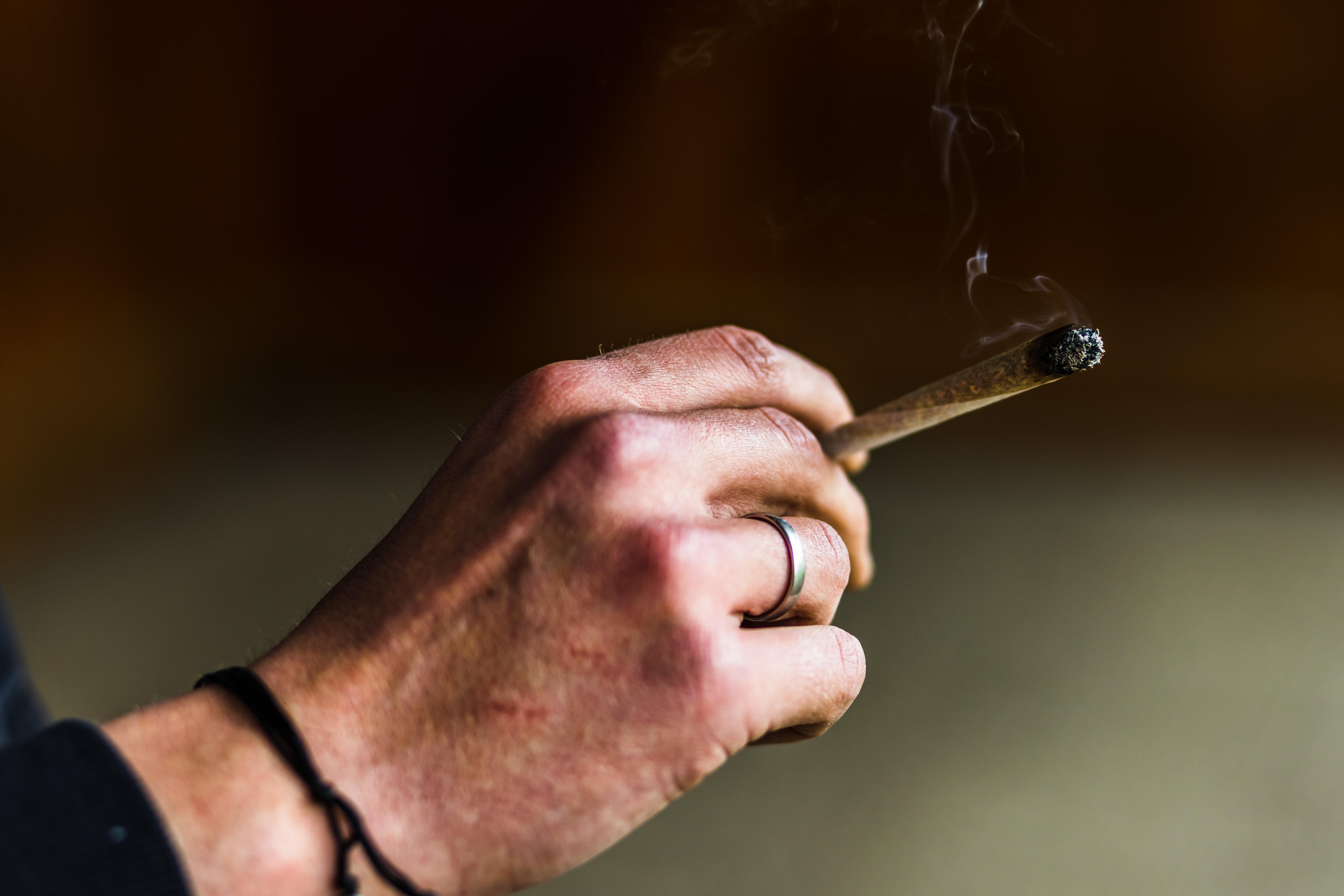 Ein Mensch hält einen brennenden Joint in der Hand. 