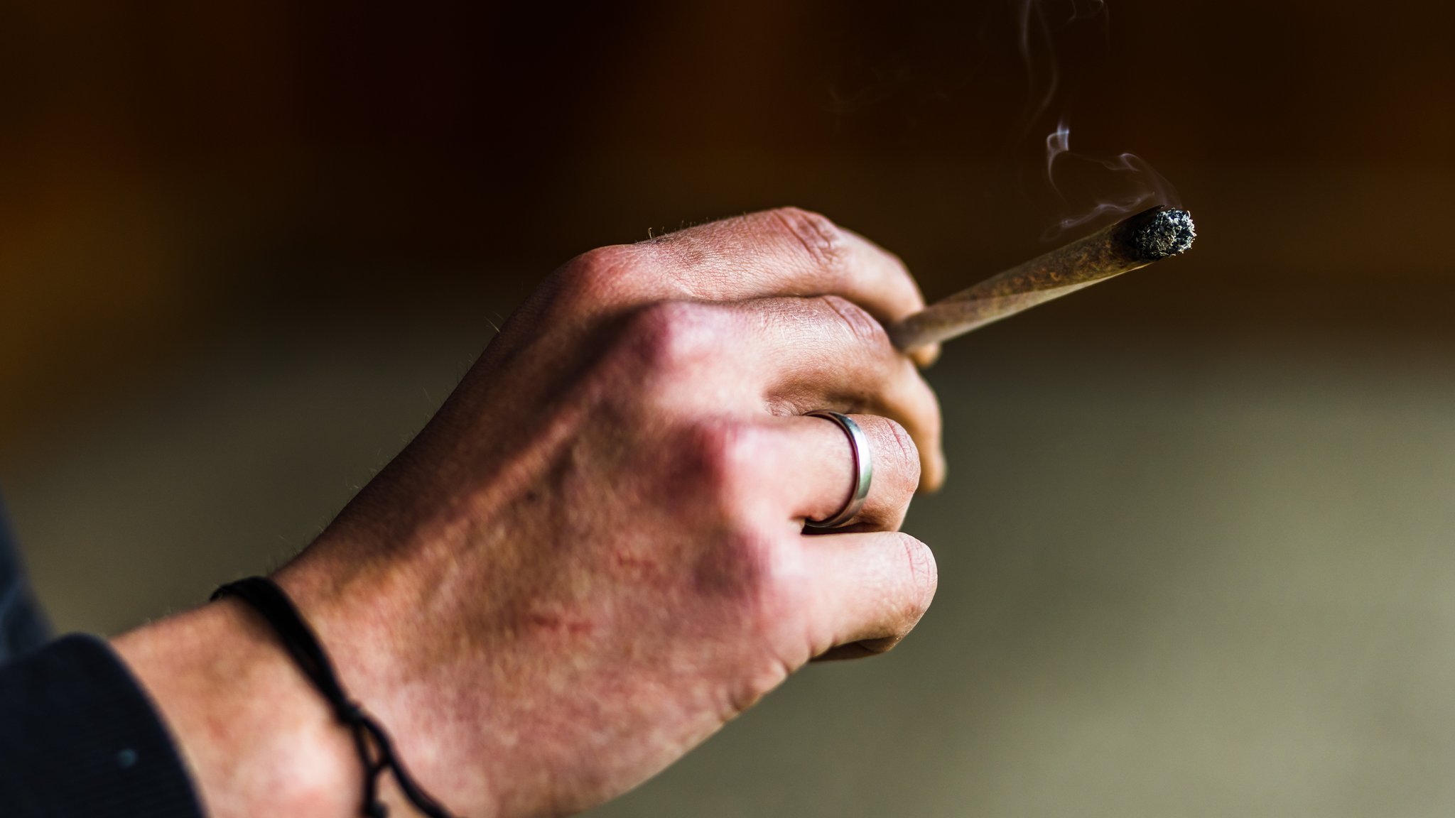 Ein Mensch hält einen brennenden Joint in der Hand. 