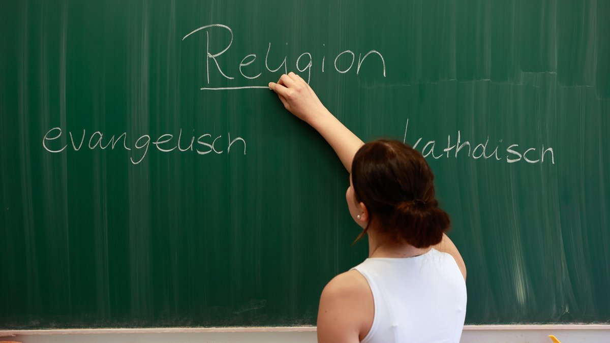 Eine Lehrerin unterteilt den Religionsunterricht an der Tafel in "katholisch" und "evangelisch". 
