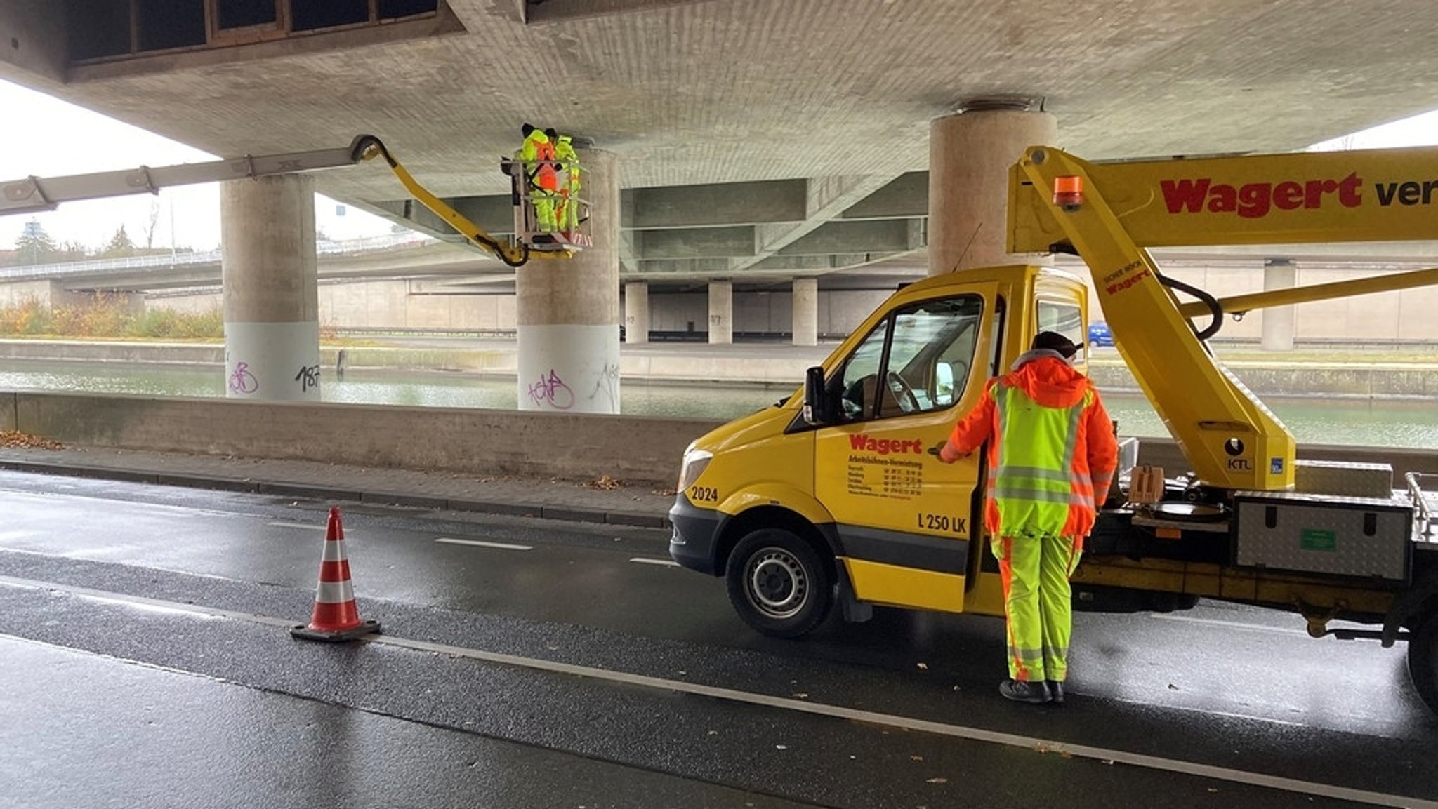 Unter einer Brücke steht ein Wagen mit Hebebühne, Arbeiter inspizieren die Unterseite des Bauwerks. | Bild: BR/Andi Heinicke Unter einer Brücke steht ein Wagen mit Hebebühne, Arbeiter inspizieren die Unterseite des Bauwerks.