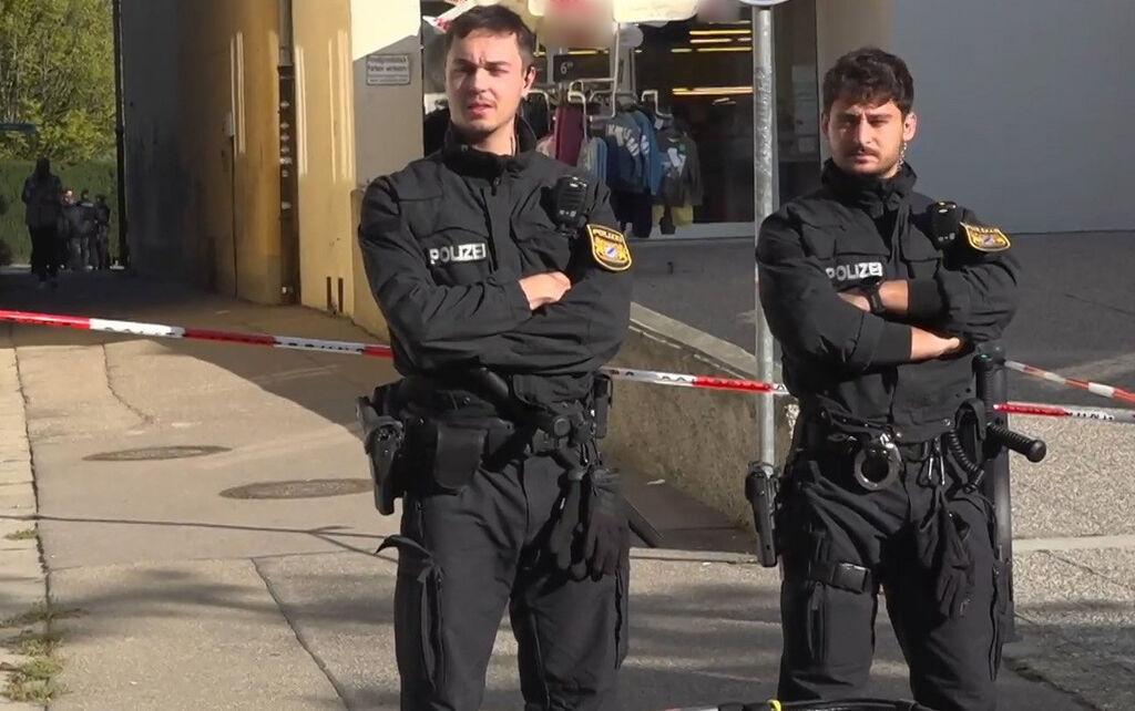 02.10.2025, Bayern, Friedberg: Zwei Polizisten sind in der Nähe einer Schule im Einsatz und sperren einen Zugang. Im schwäbischen Friedberg hat die Polizei an einer Schule einen Verdächtigen festgenommen. Wie eine Polizeisprecherin berichtet, wurden die Beamten wegen einer Körperverletzung alarmiert. Ob tatsächlich jemand im Bereich der Mittelschule verletzt wurde, war allerdings zunächst unklar. Foto: Jason Tschepljakow/dpa - ACHTUNG: Firmenauschriften (hinten) wurde(n) aus rechtlichen Gründen gepixelt +++ dpa-Bildfunk +++