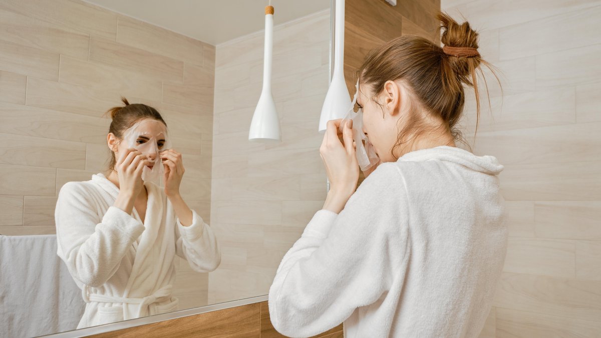 Frau in Badezimmer trägt eine Hautpflegemaske auf ihr Gesicht 