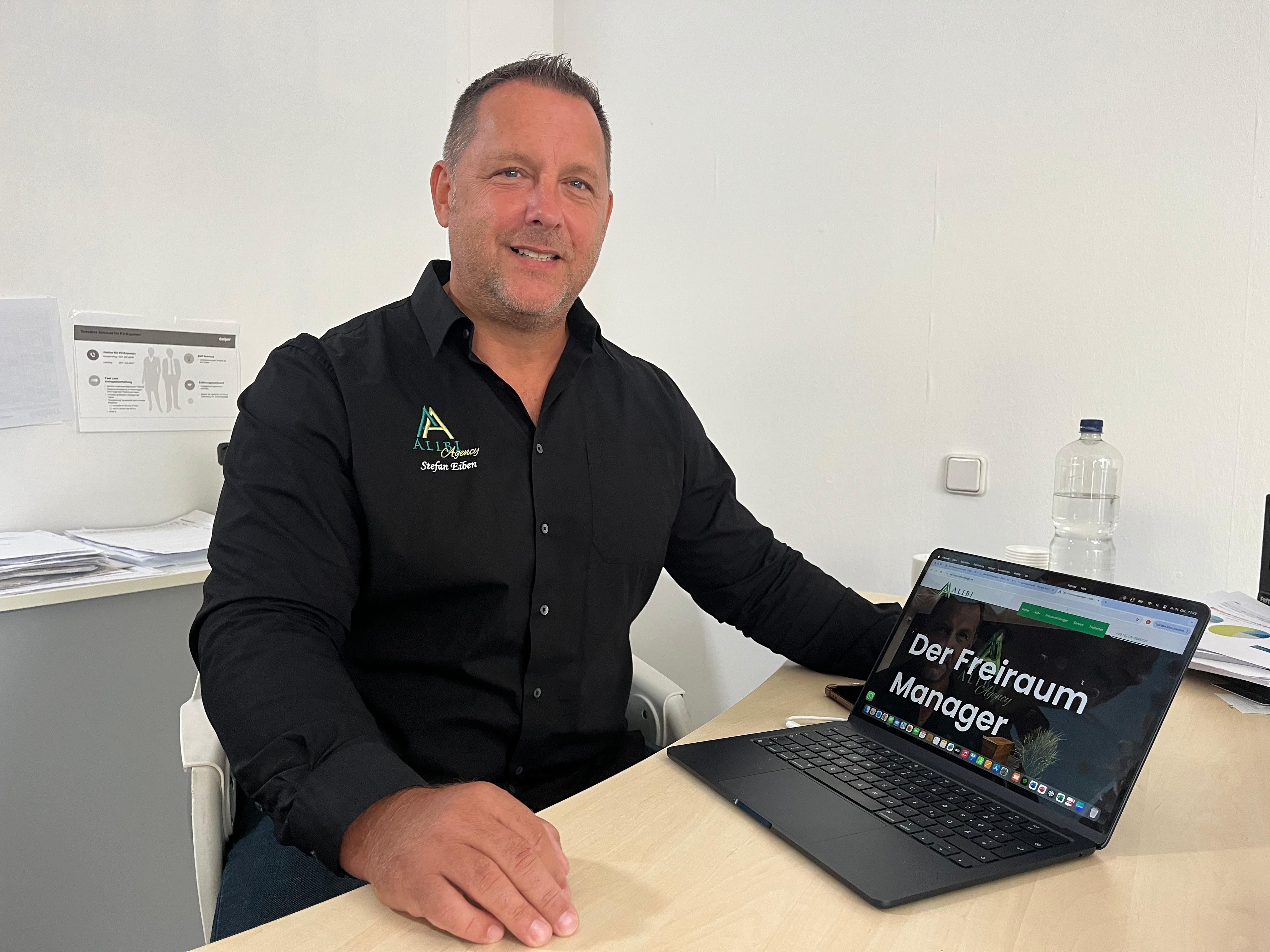Stefan Einen sitzt im schwarzen Hemd an seinem Schreibtisch am Laptop. 